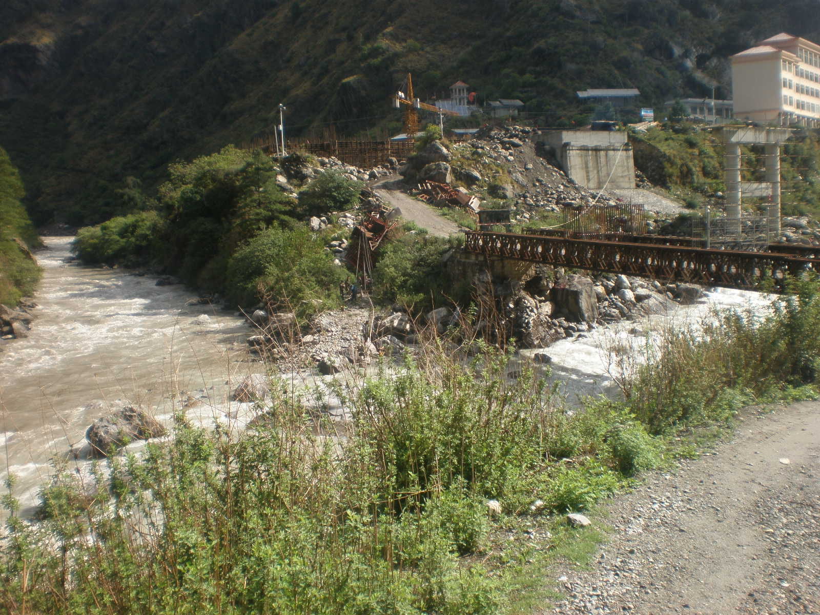 The Bhotekoshi–Trishuli river running fast past a steel bridge and a road cut into the hillside